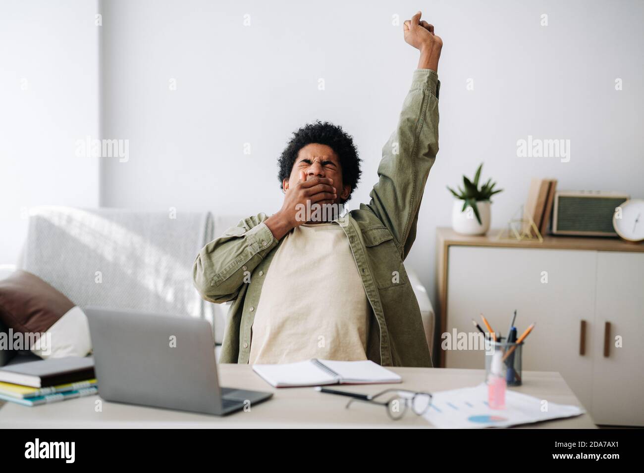 Tired black student yawning and stretching during his remote studies from home Stock Photo