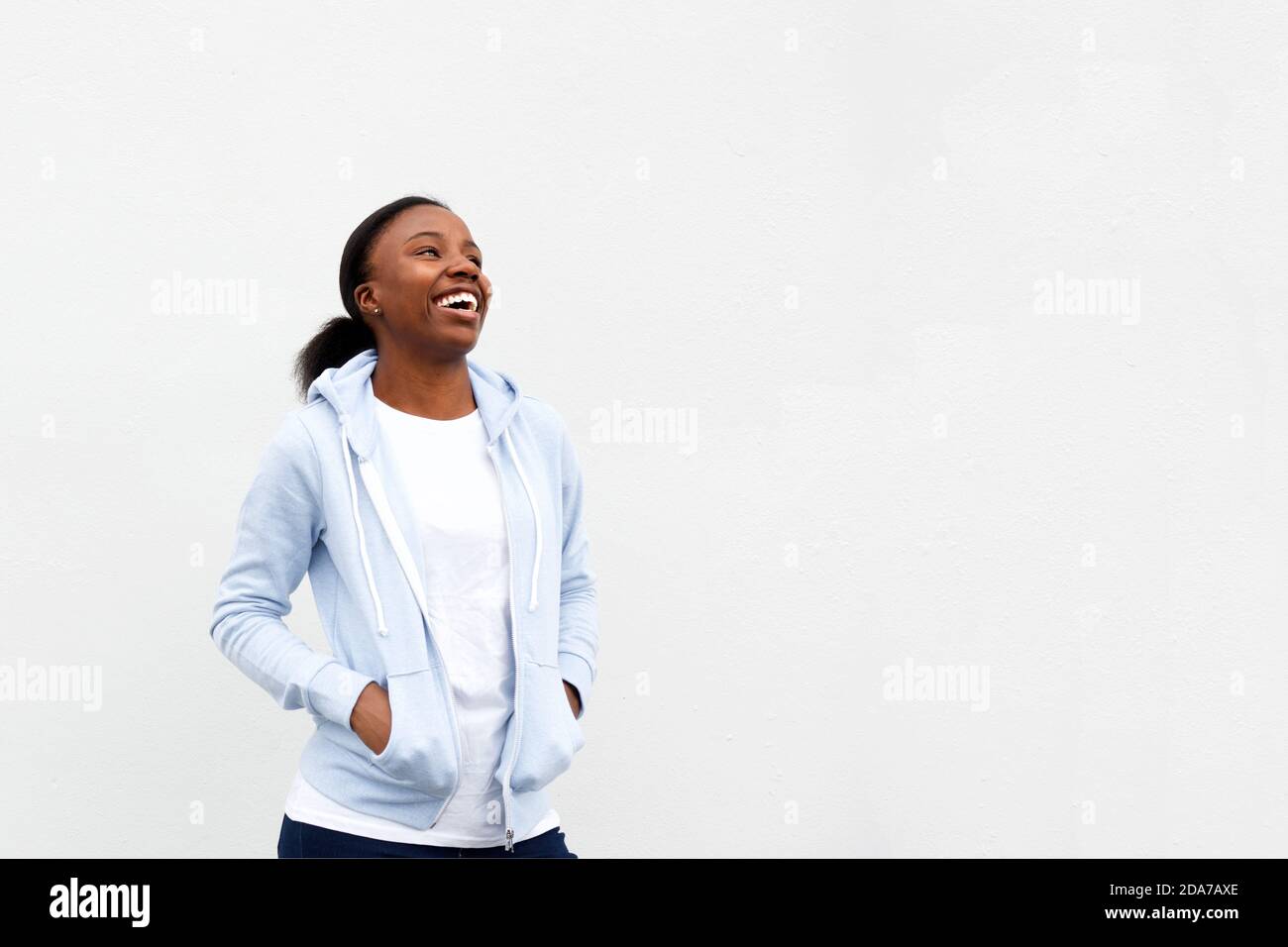 Portrait of happy african woman standing with hands in pockets laughing ...