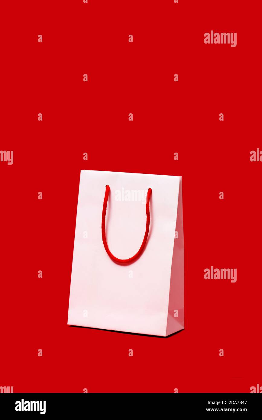 a white paper shopping bag with red handles on a red background, with ...