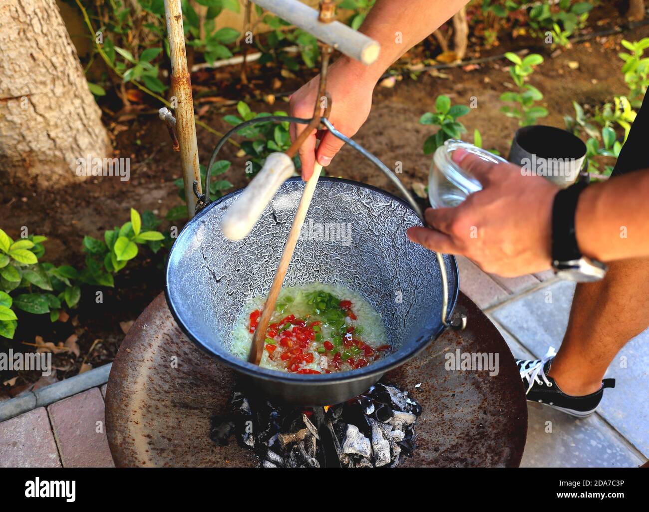 Making Hungarian gulyas leves, goulash, in a cauldron, bogracs, in the garden - cooking the onions and peppers Stock Photo