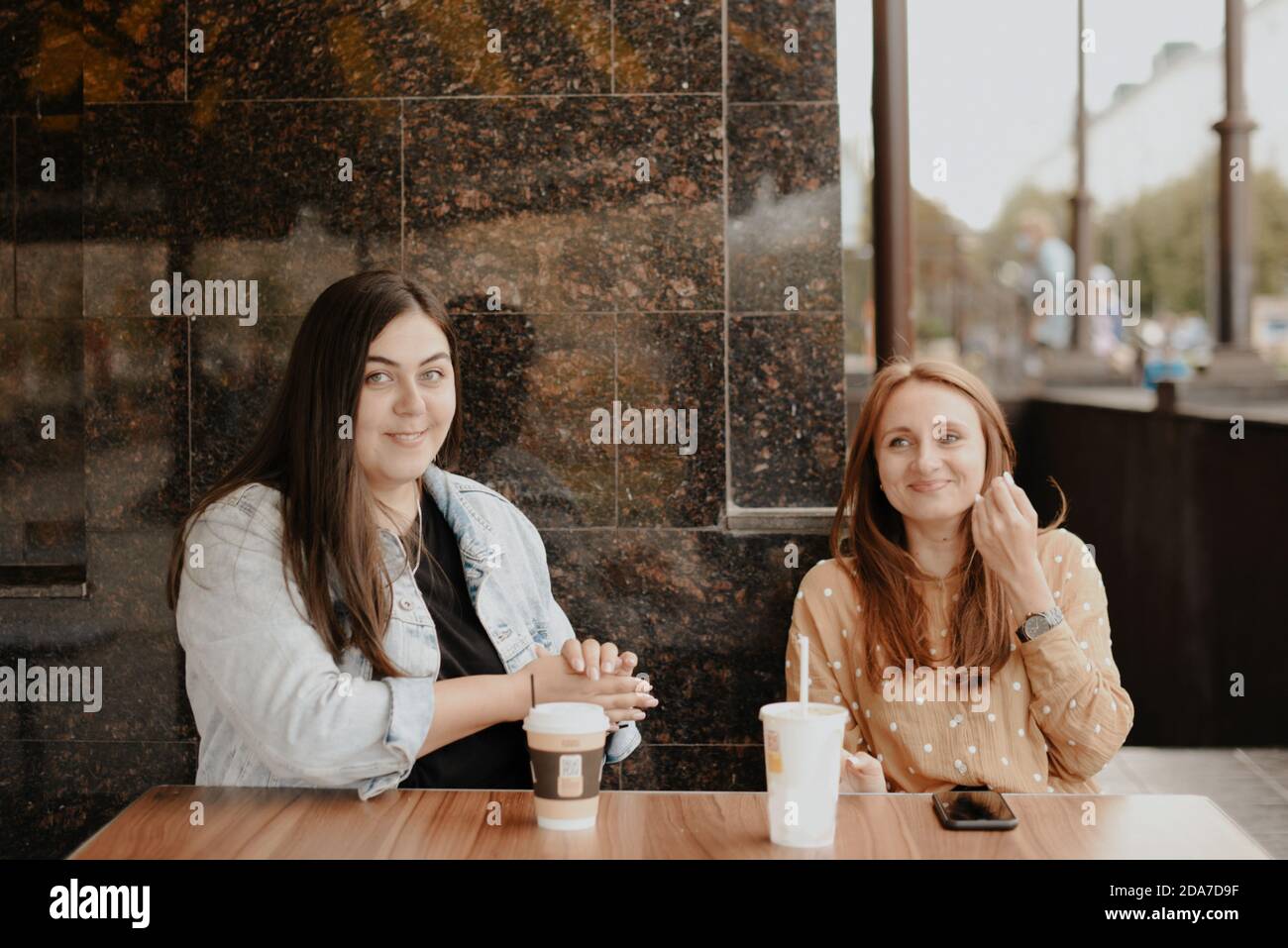 Two young women sit in an open cafe in the city 1 Stock Photo - Alamy