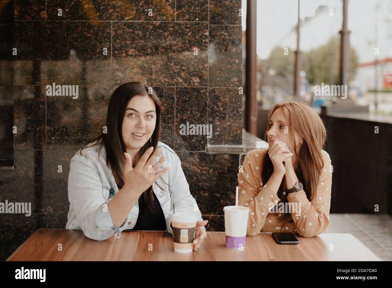 Two young women sit in an open cafe in the city 1 Stock Photo - Alamy