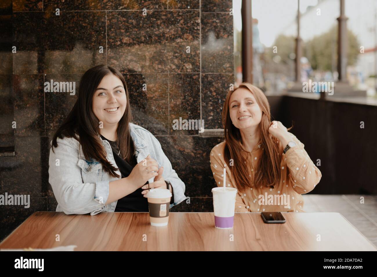 Two young women sit in an open cafe in the city 1 Stock Photo - Alamy