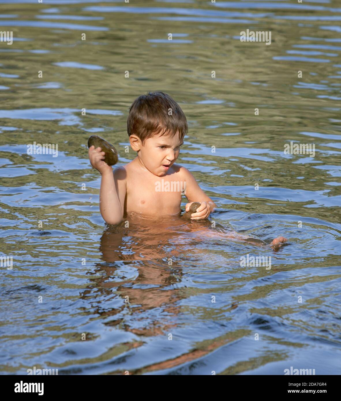 Boy sits in the river and played with a stone Stock Photo