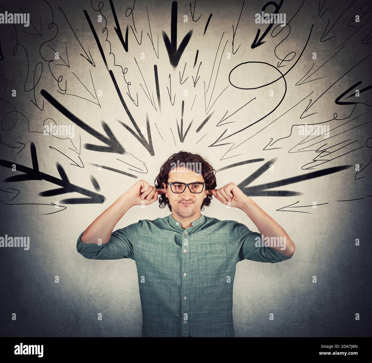 Irritated and annoyed man covering ears with fingers, looks displeased, refuses to listen gossips. Frustrated guy under pressure as multiple arrows po Stock Photo