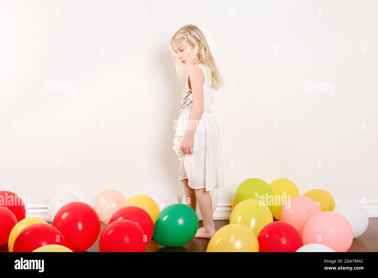 Sad upset little girl celebrating birthday at home alone. Lovely lonely unhappy girl child with colorful balloons. Quarantine birthday party at home Stock Photo