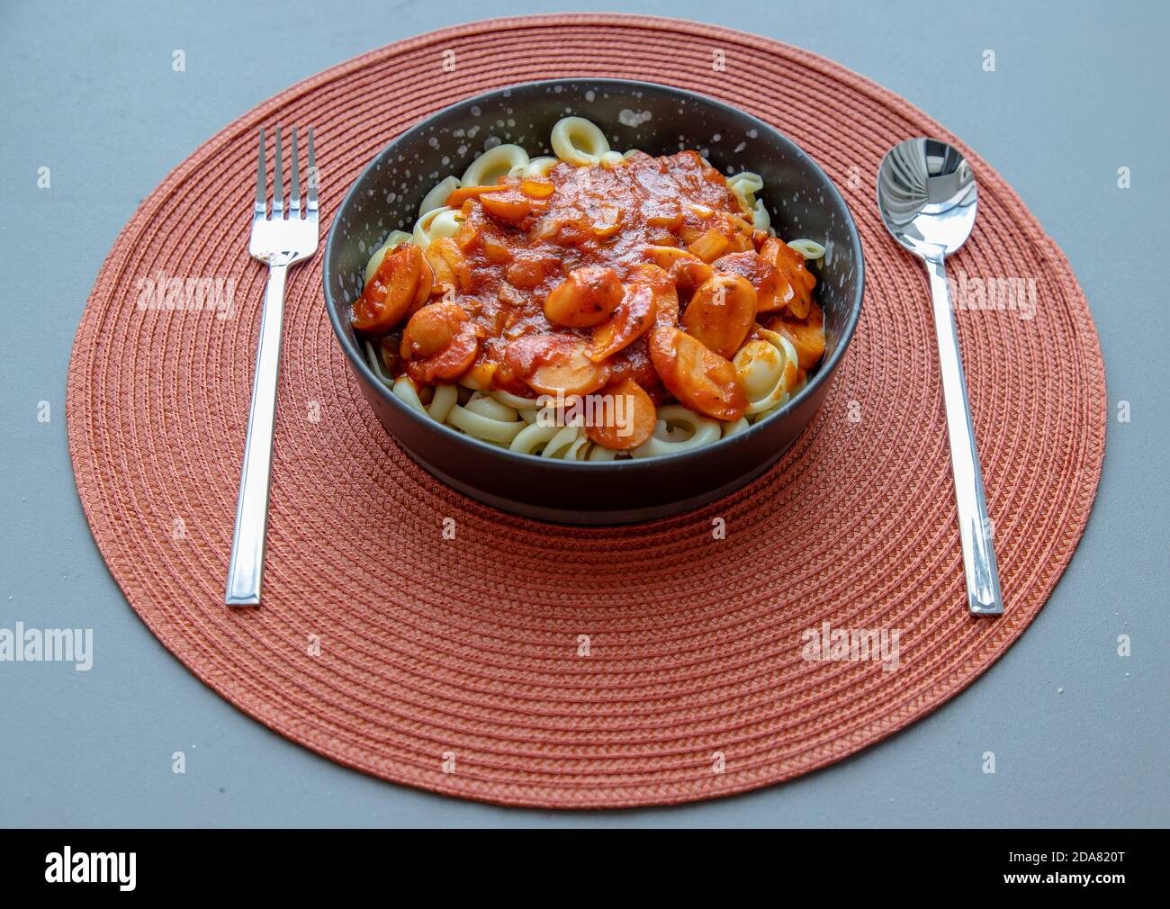 Dischi pasta with sausage, onion and balognese sauce in a black plate on red background. Copy space, No focus, specifically. Stock Photo