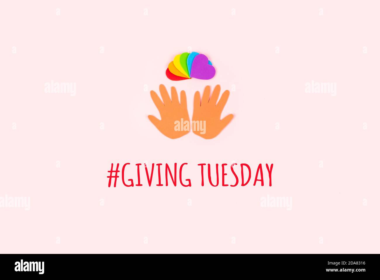 Giving tuesday concept. Minimal flat lay with text Giving Tuesday paper palms and rainbow hearts on pastel background. Stock Photo
