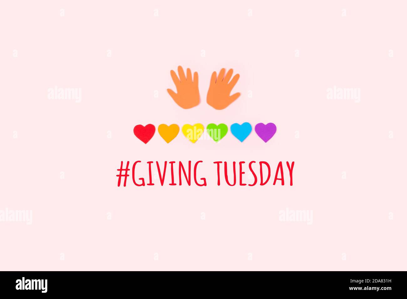 Giving tuesday concept. Minimal flat lay with text Giving Tuesday paper palms and rainbow hearts on pastel background. Stock Photo