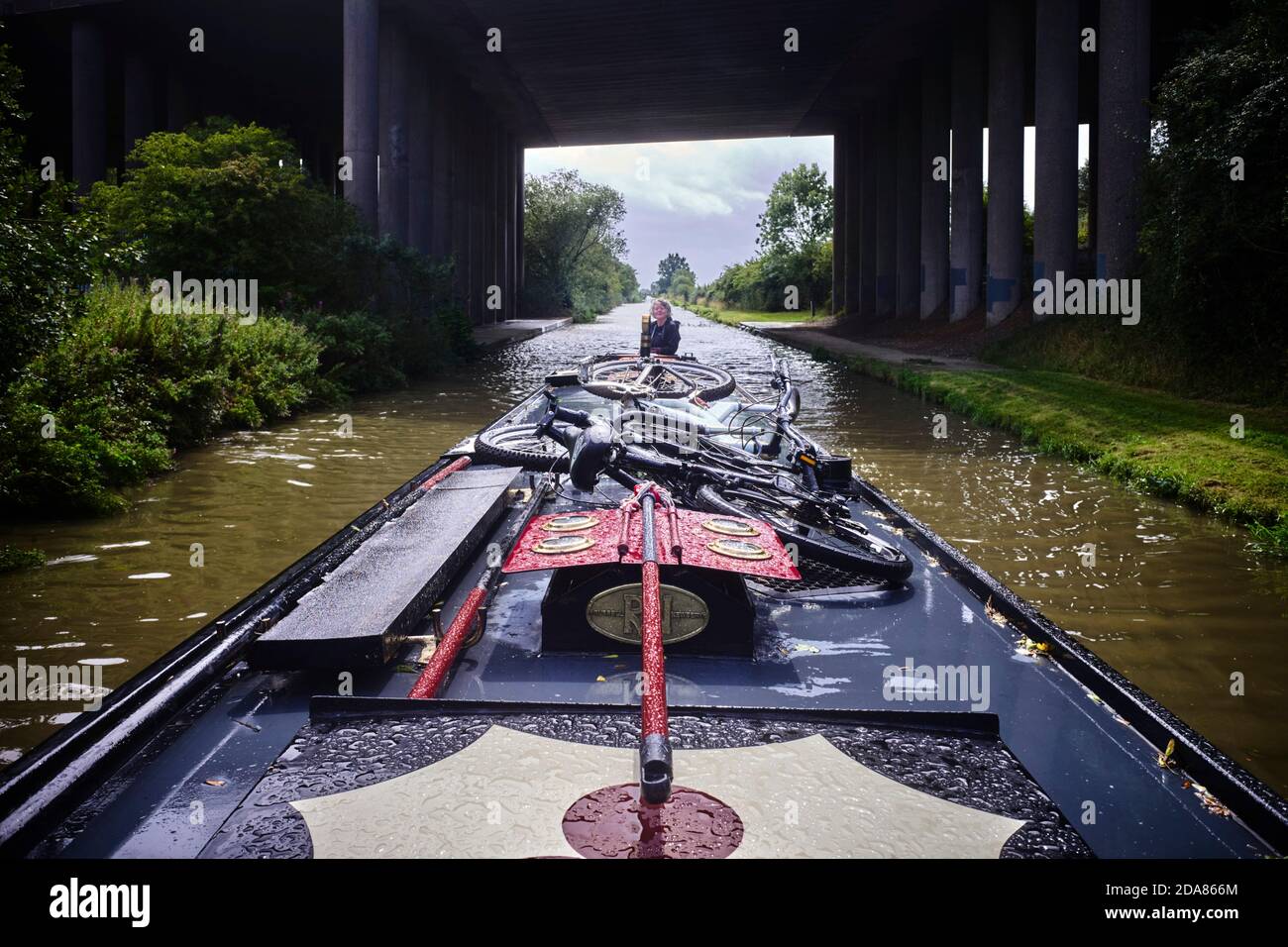 Narrowboat under a motorway bridge having just been through a heavy shower of rain near Braunston on the Grand Union Canal Stock Photo