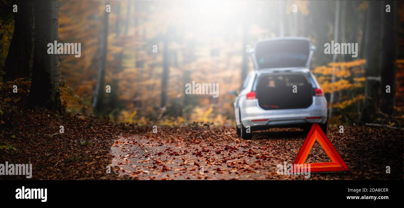 Car triangle on a autumn road. Problem with car on a morning autumns forest road covered of fall leave. Panorama or Banner broken car concept. High quality photo Stock Photo