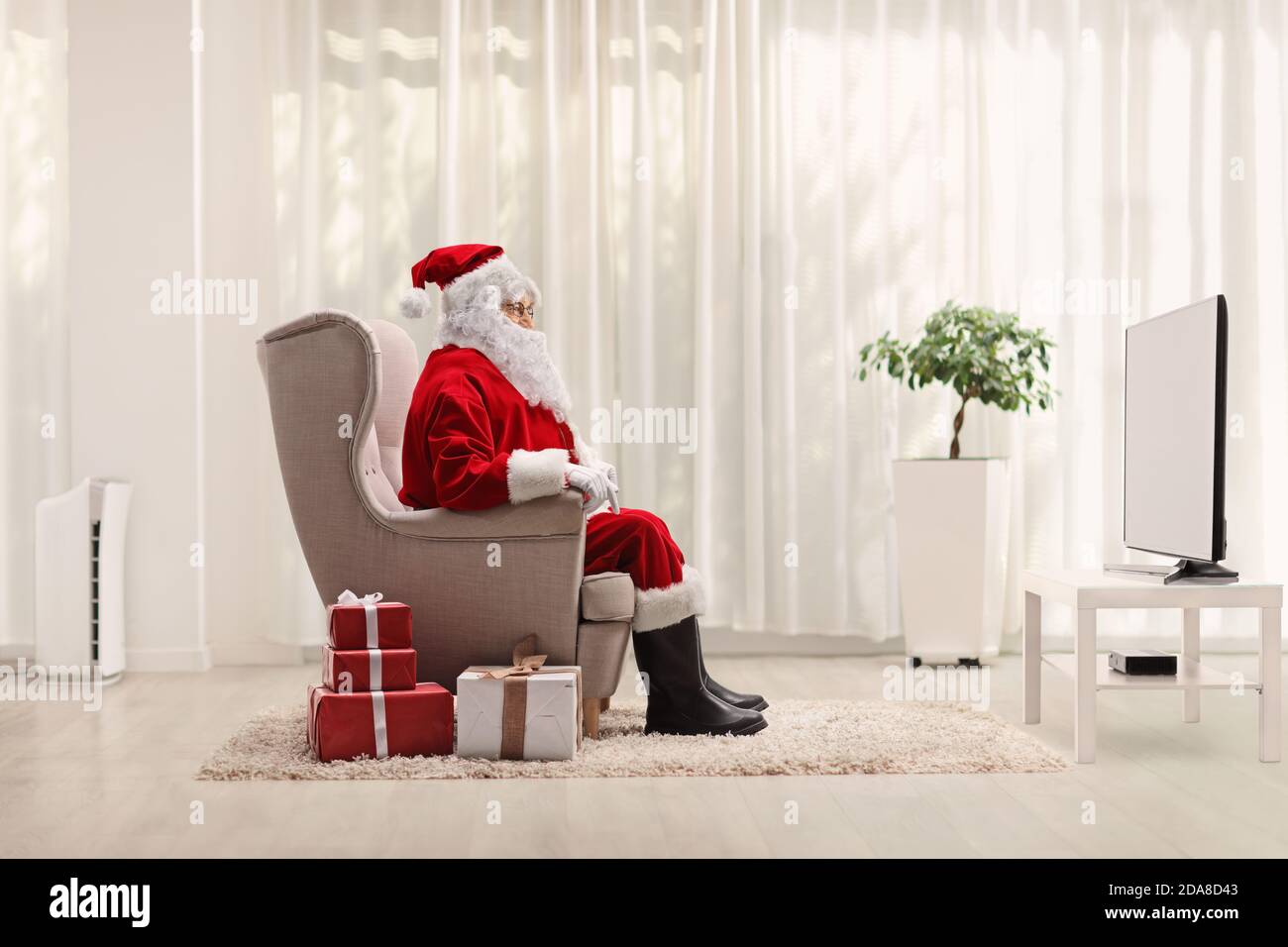Santa claus sitting in an armchair and watching tv at home Stock Photo
