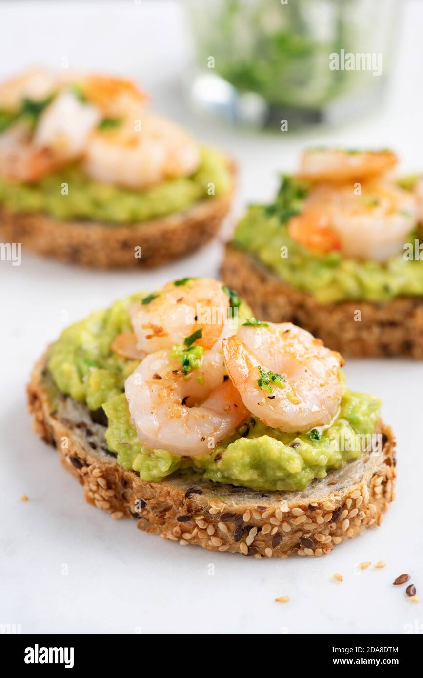 Bruschetta with avocado cream and shrimps on white marble background, closeup view. Appetizer or snack avocado toasts with prawn Stock Photo