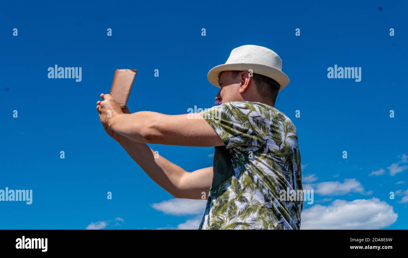 The guy takes pictures on the blue background of the sky and white clouds Stock Photo