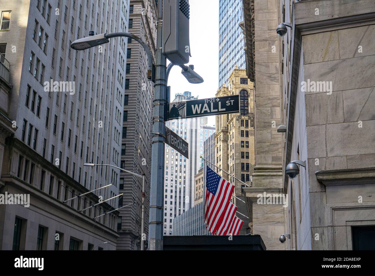 New York City, NY/USA - November 8 2020: Road sign of New York Wall street at the corner Broad street. American flag hanging from the New York Stock E Stock Photo