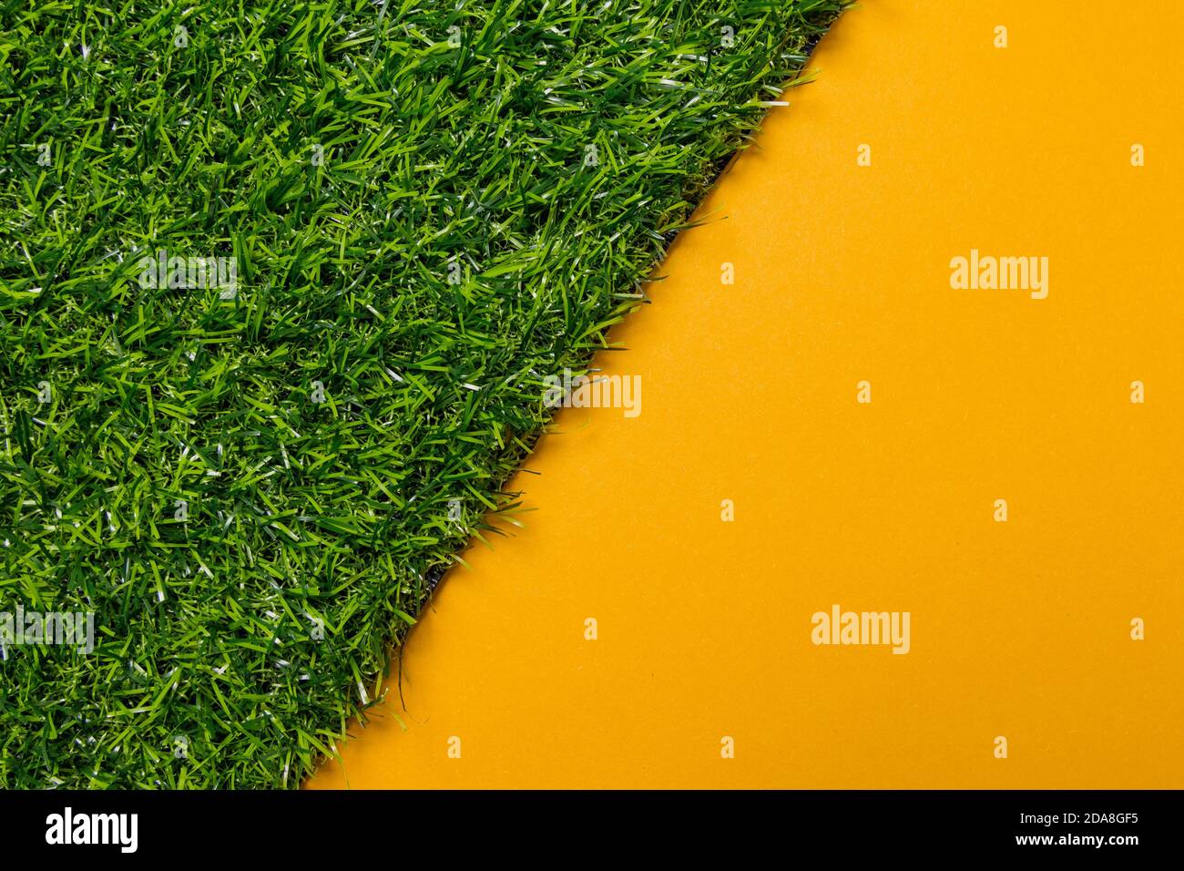 Top view of artificial grass on a yellow uniform background, the image is cut diagonal by the plastic gras, use as template or background Stock Photo