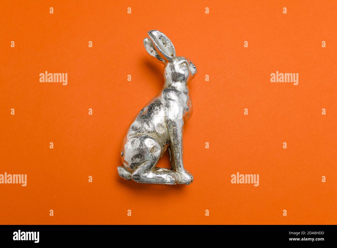 Side view of a silver metallic easter bunny figure on a red uniform background with light soft shadows, use as easter virtual meeting background. Stock Photo