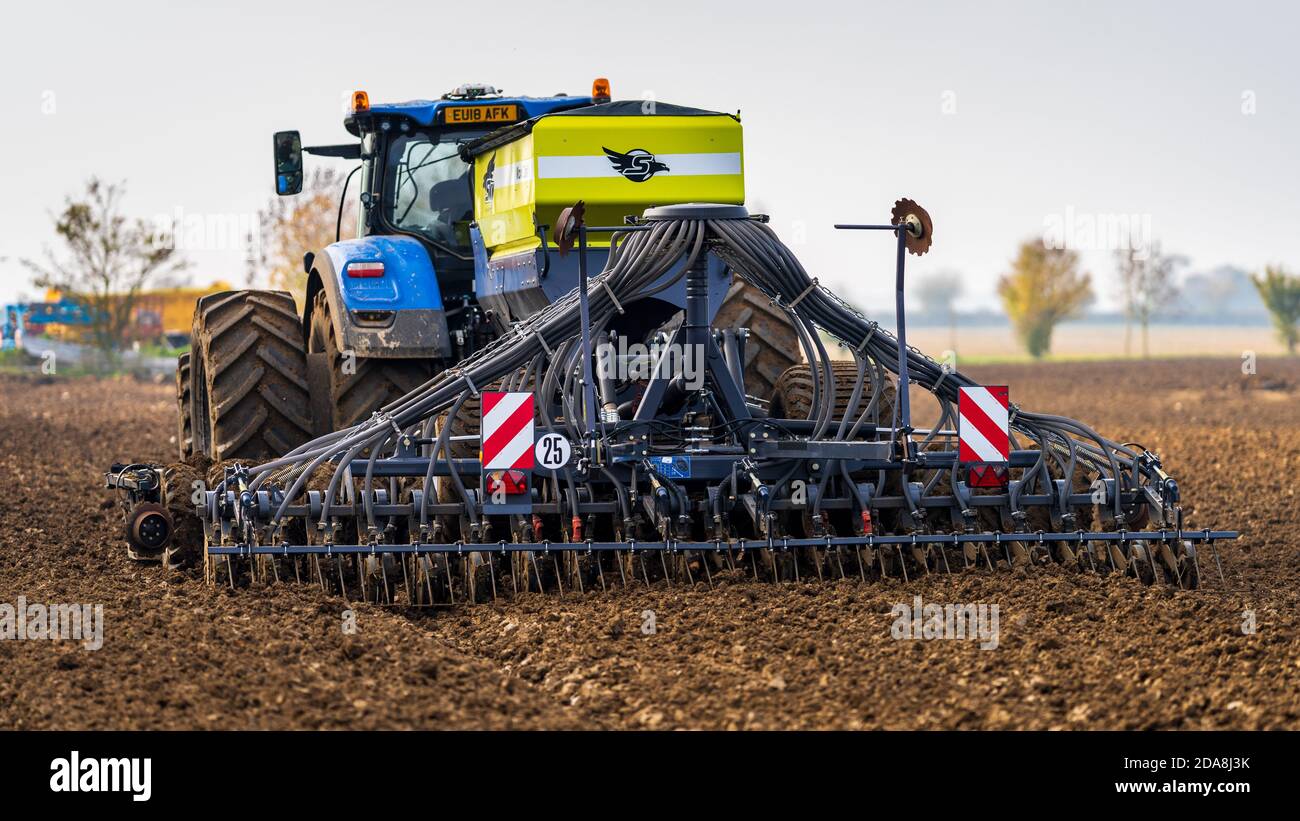 A tractor with towed seed drill or planter to efficiently plant seeds at the optimum depth and spacing. Stock Photo