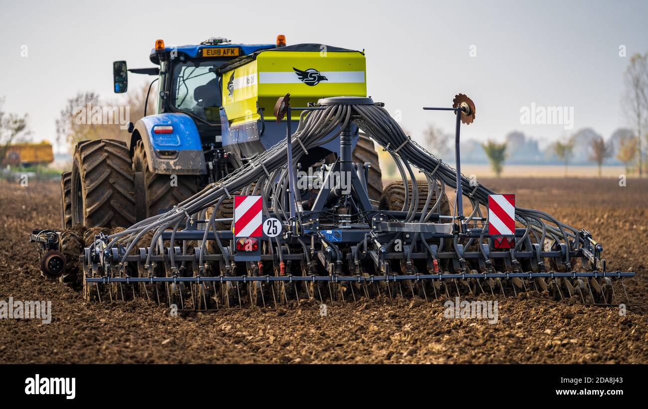 A tractor with towed seed drill or planter to efficiently plant seeds at the optimum depth and spacing. Stock Photo
