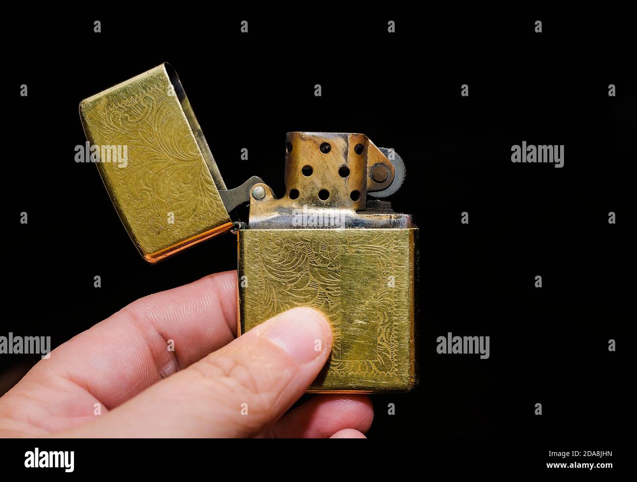 A hand holds a gold Zippo lighter open and unlit. Zippo