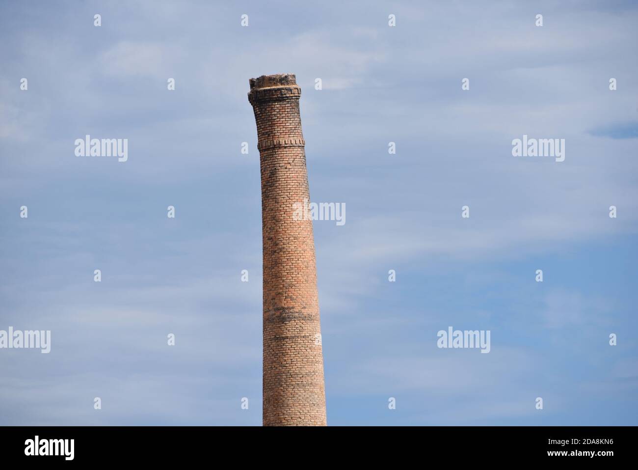An old brick chimney leans defiantly against a mottled blue sky, in this photo taken in Oliva, Spain Stock Photo