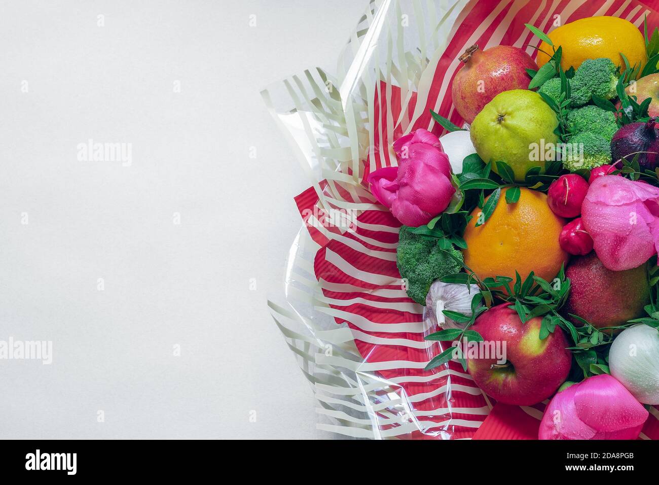 The arrangement of fruit, vegetables, flowers and green leaves surrounded by ornate red and white translucent striped paper on a white background Stock Photo