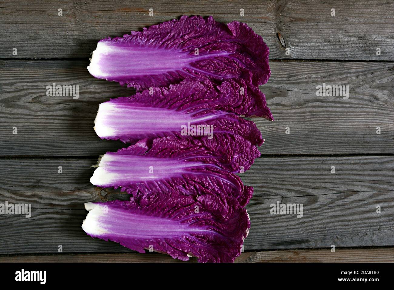 Fresh leaves of purple Chinese cabbage on a wooden background. Flat lay. Purple Chinese cabbage leaf, lettuce leaves. Seasonal vegetables, top view. Stock Photo