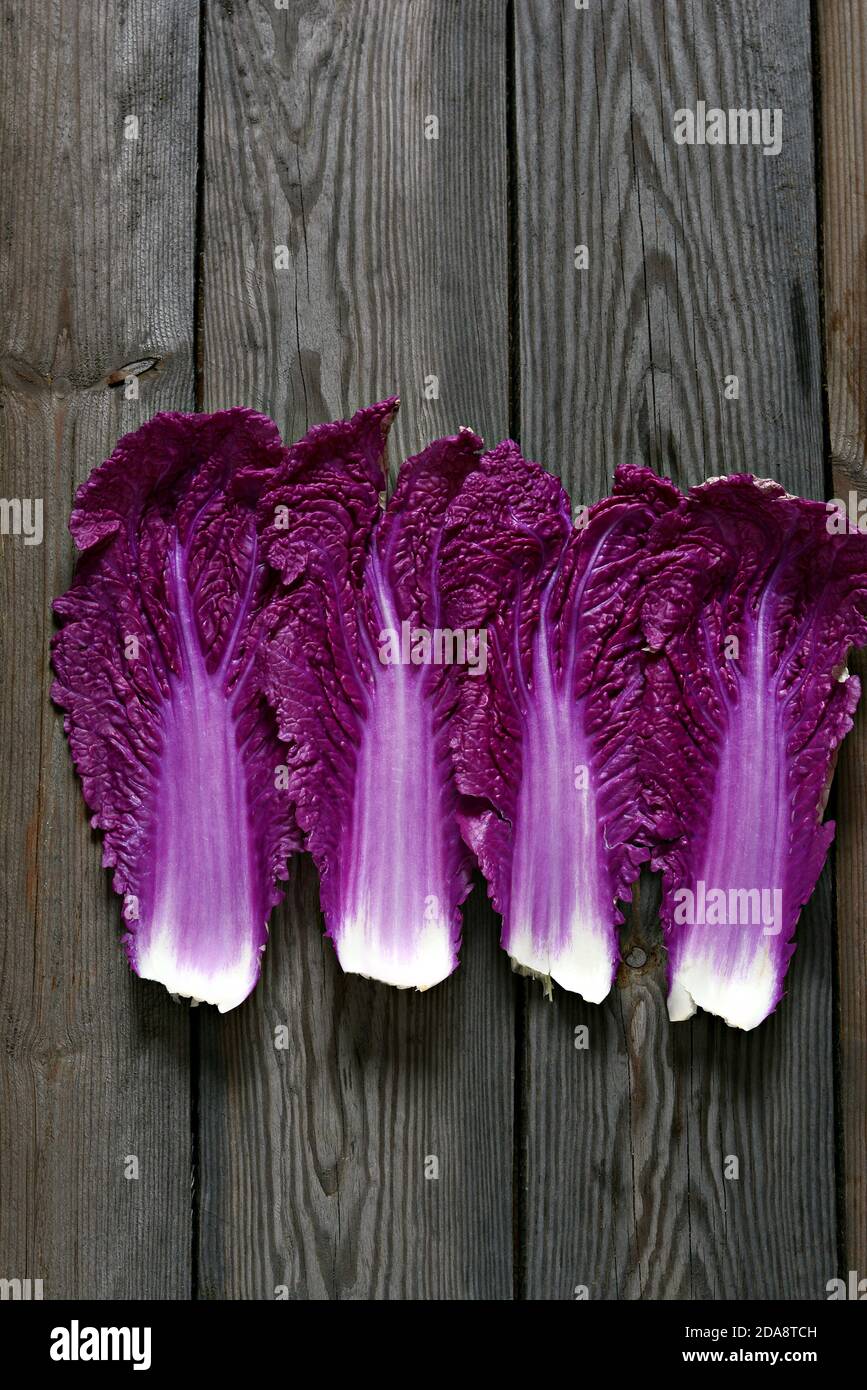 Fresh leaves of purple Chinese cabbage on a wooden background. Flat lay. Purple Chinese cabbage leaf, lettuce leaves. Seasonal vegetables, top view. Stock Photo