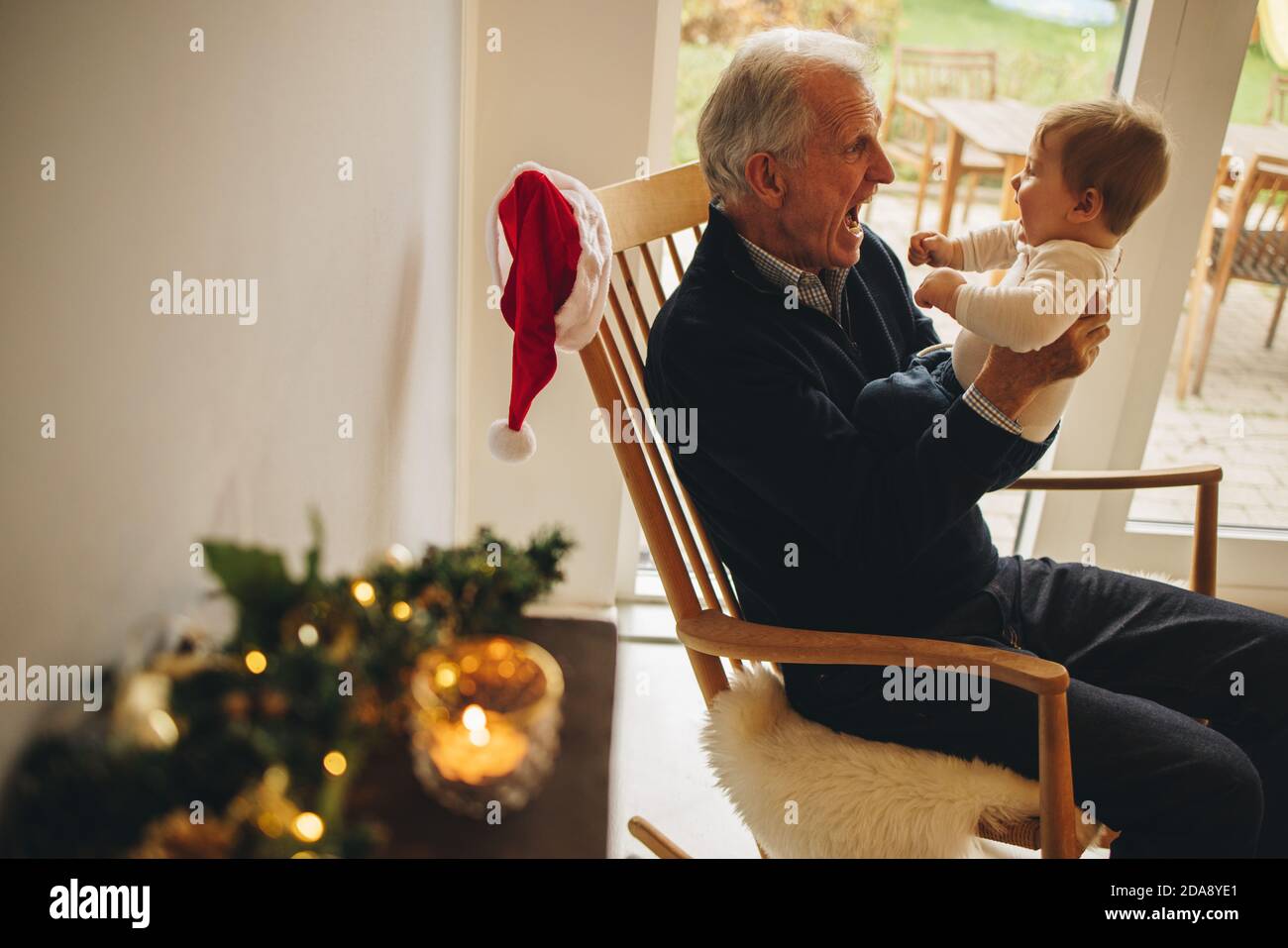 Senior man having fun with small boy at home during christmas. Grandfather sitting on chair playing with his grandson. Stock Photo