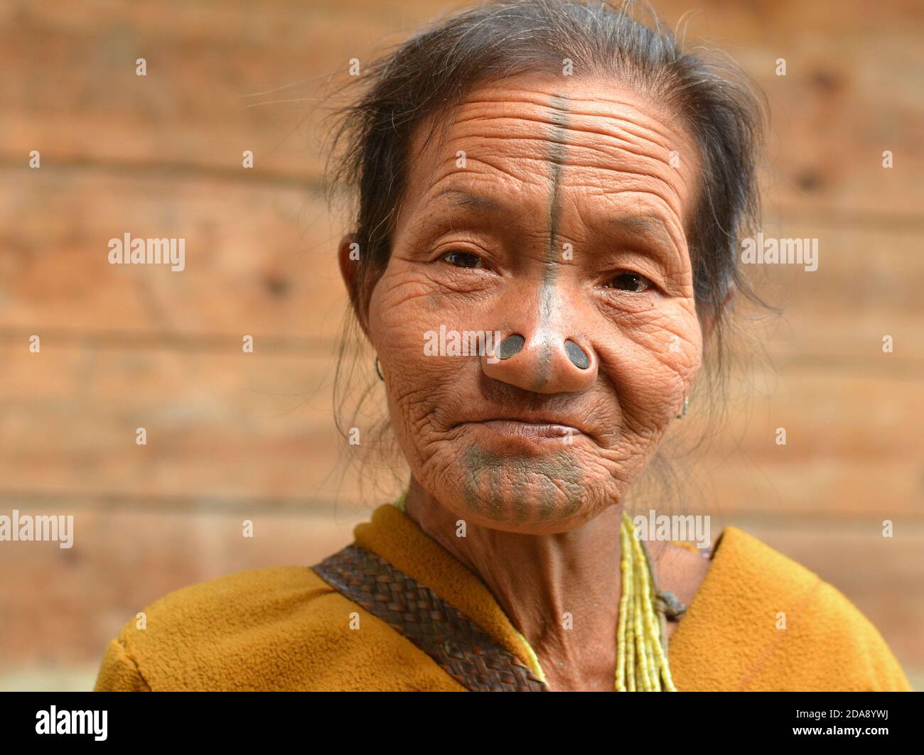 Old Northeast Indian Apatani ethnic minority tribal woman with black wooden nose plugs and traditional face tattoos poses for the camera. Stock Photo