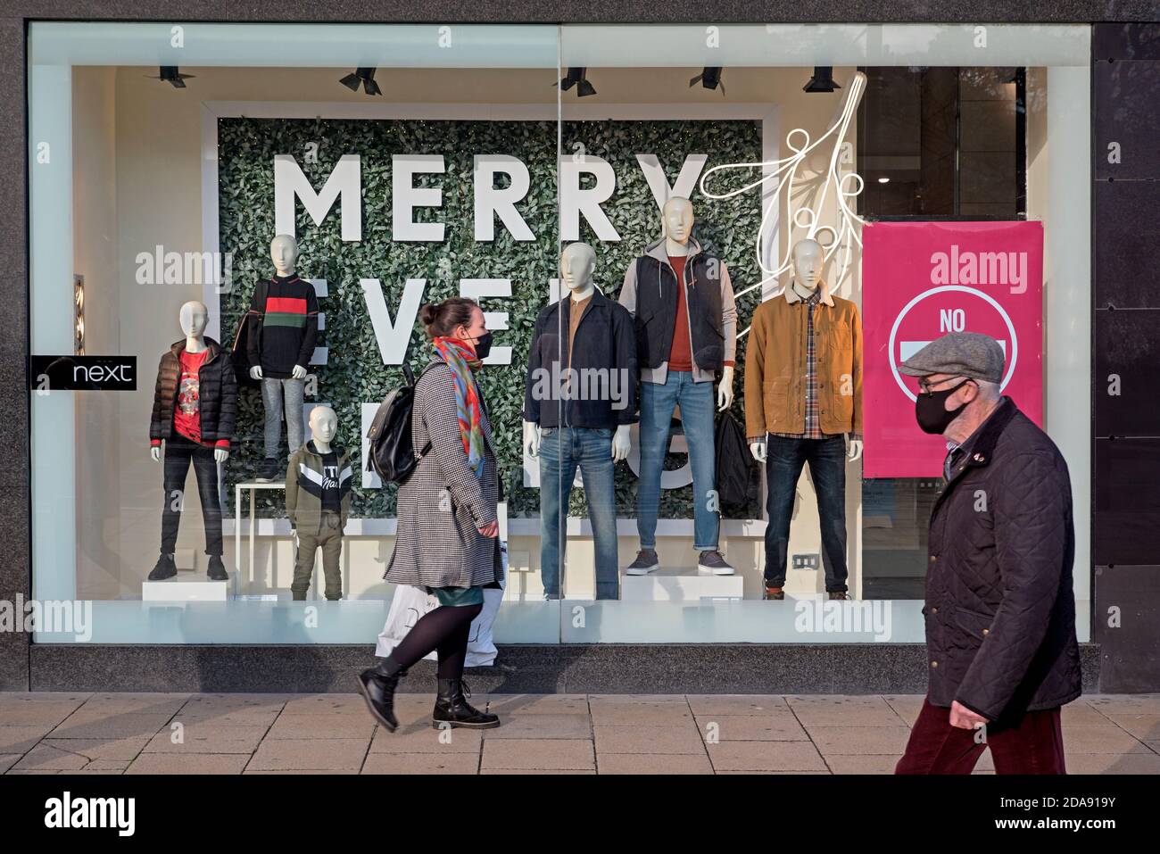 Shoppers wearing face masks walk by the window display of the Next store on Princes Street, Edinburgh, Scotland, UK. Stock Photo