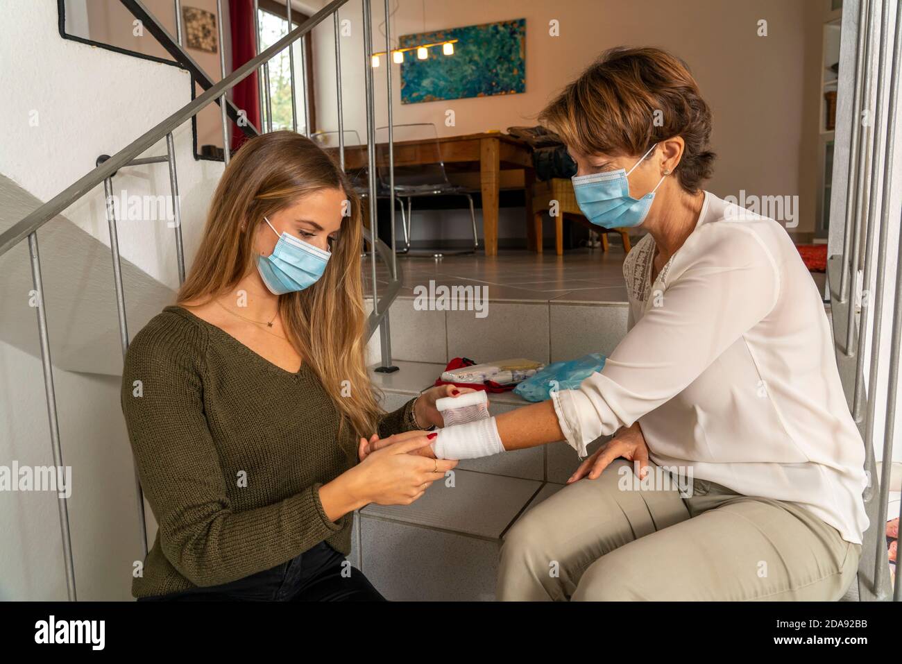 First aid measures under corona conditions, application of a bandage, after an accident in the home, with a nose-and-mouth mask, when giving first aid Stock Photo