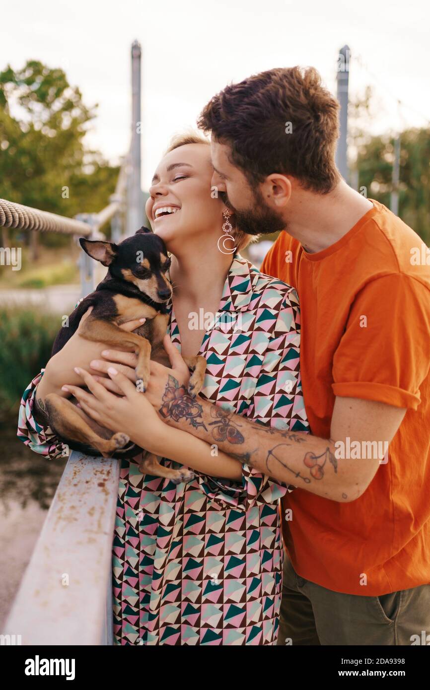 Happy smiling young couple hugging their dog on bridge Stock Photo - Alamy