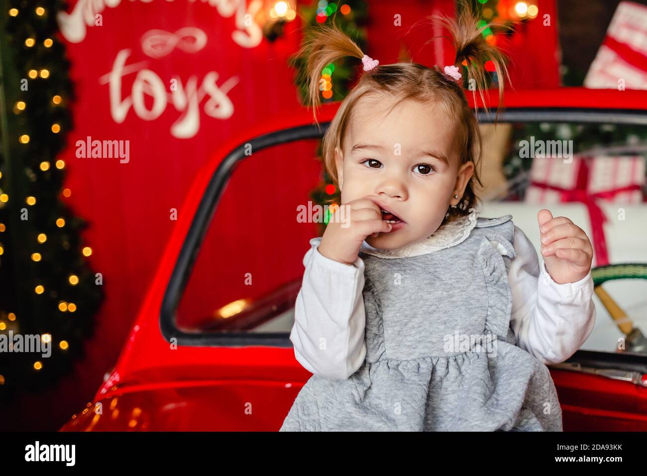 Joyful baby sitting on red Christmas car in the living room at home. Copy space. Stock Photo