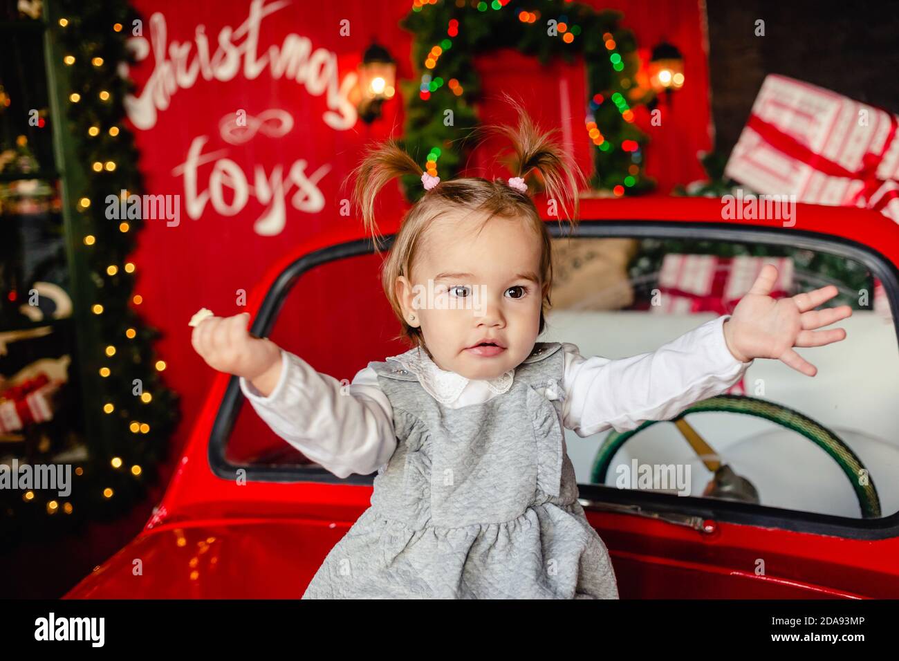 Joyful baby sitting on red Christmas car in the living room at home. Merry Christmas and Happy Holidays! Stock Photo