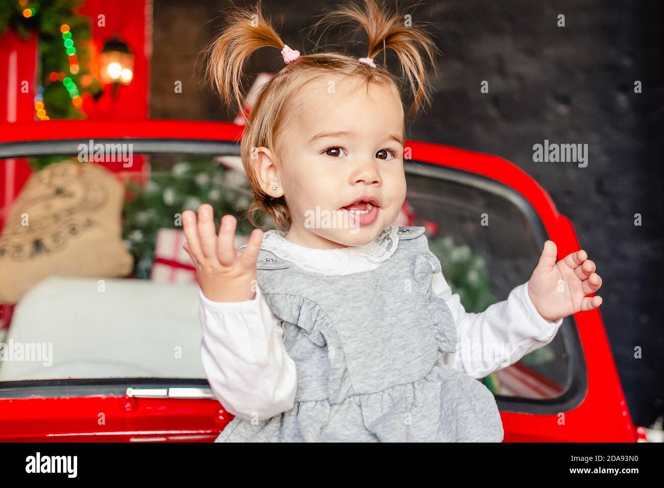 Joyful baby sitting on red Christmas car in the living room at home. Merry Christmas and Happy Holidays! Stock Photo