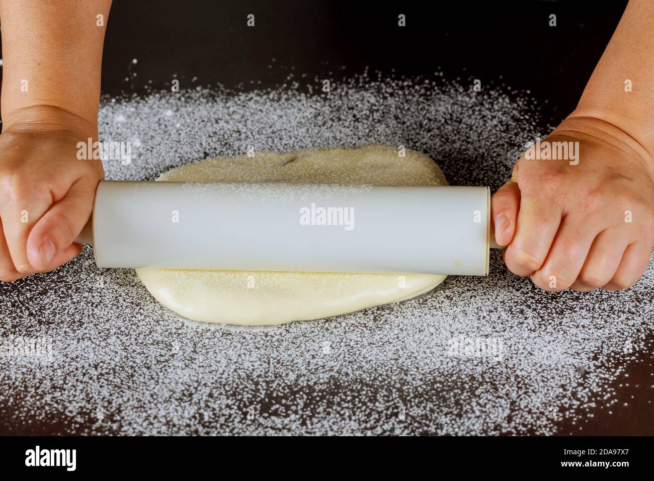 Rolling pin in woman hand and white sugar paste on table. Stock Photo