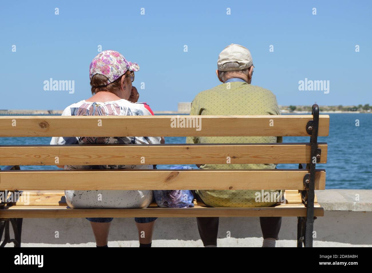 An elderly couple is sitting on a bench by the sea and admiring the ...