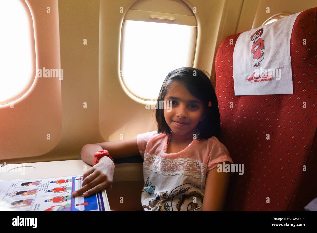 Indian airlines cabin of an Air India (AI) plane. Star Alliance Happy Indian girl traveling by an airplane. Child sitting by aircraft window India Stock Photo