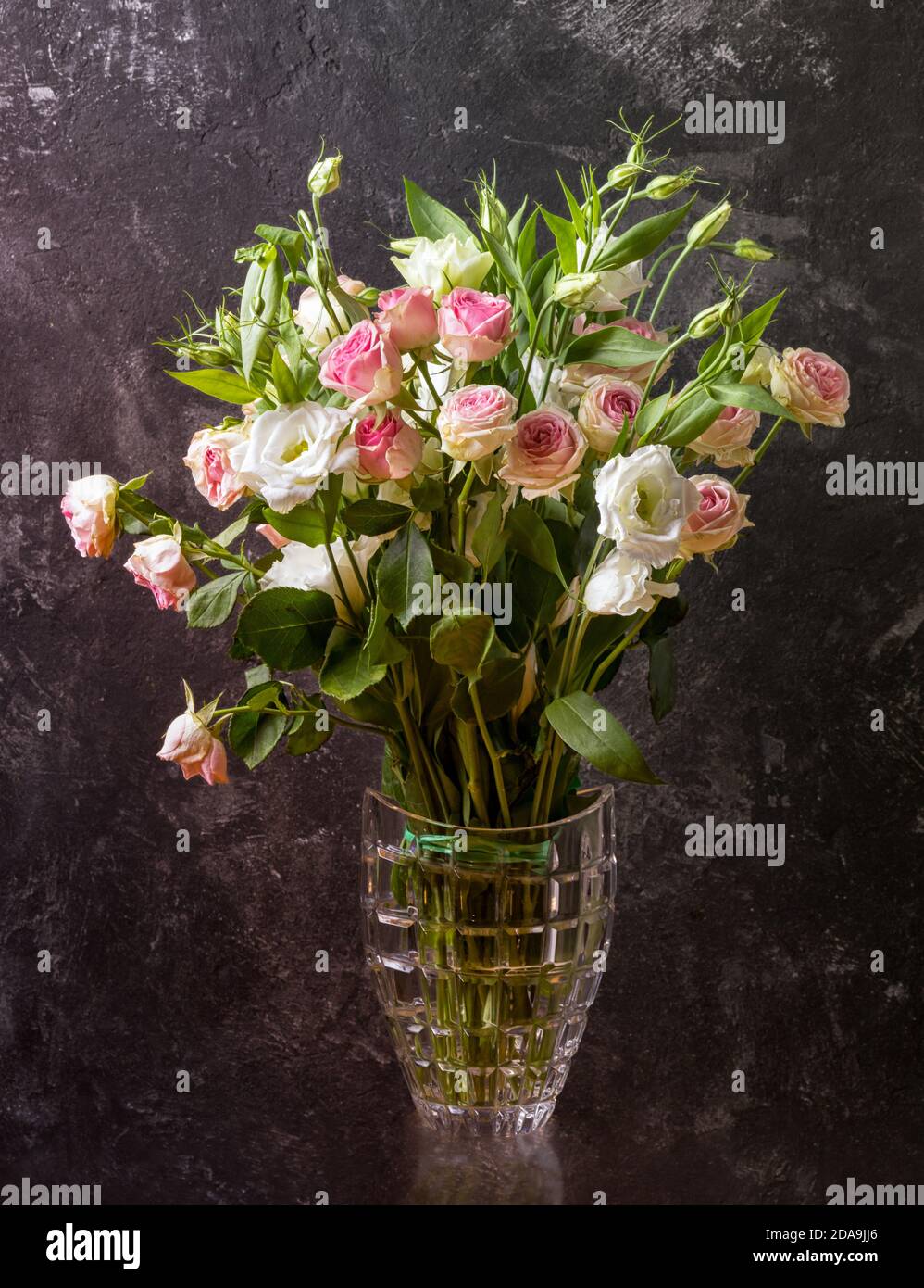 Eustoma and roses bouquet in vase on textured black wall background ...