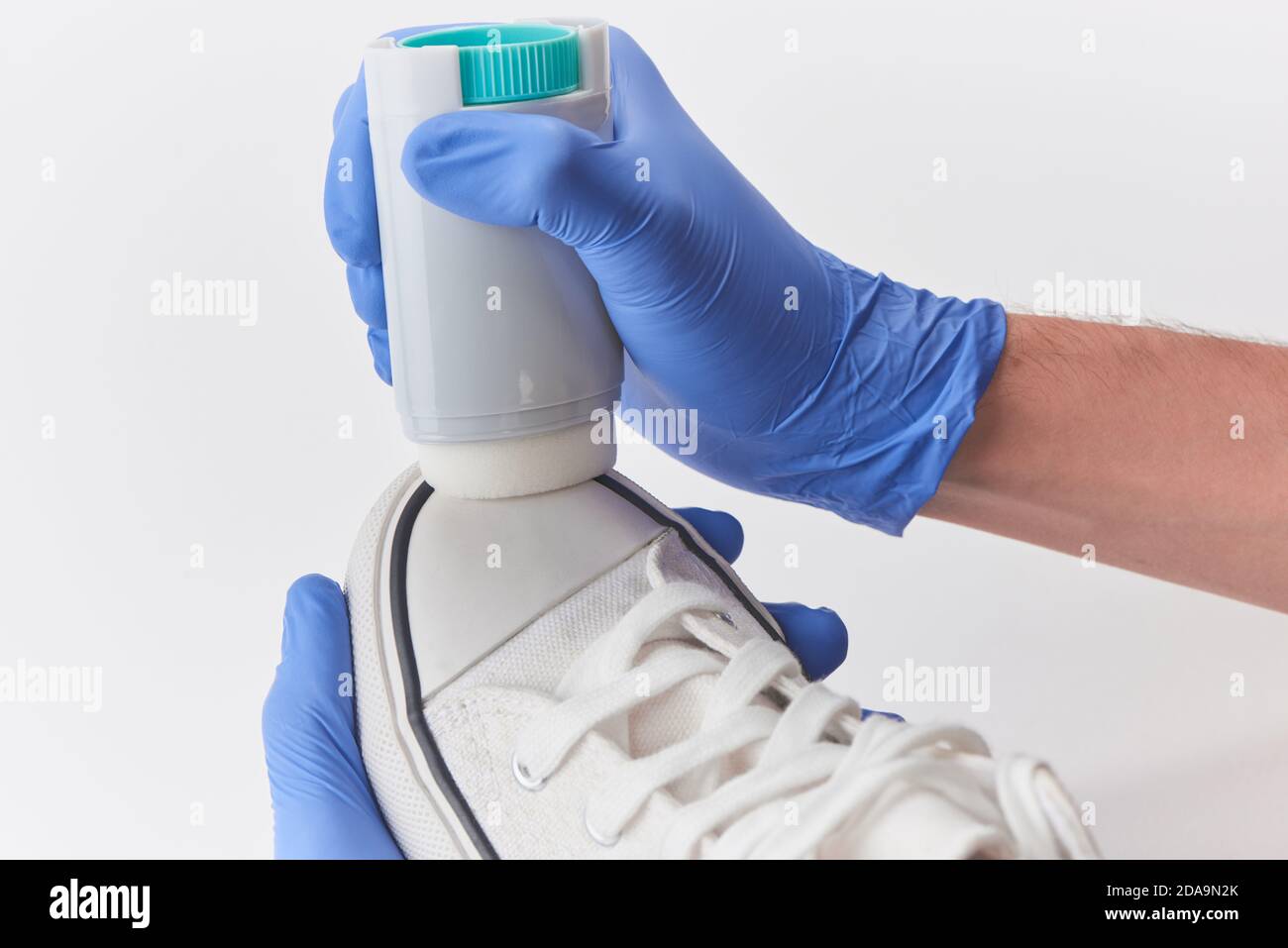 Hands in latex gloves applying white paint onto a toe cap of a canvas sneaker Stock Photo