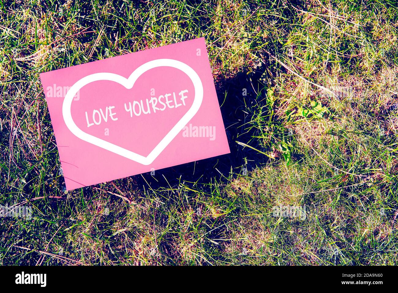 Love yourself concept written on paper with heart shape on green grass background. Inspirational quote for motivation, happiness or success in relatio Stock Photo