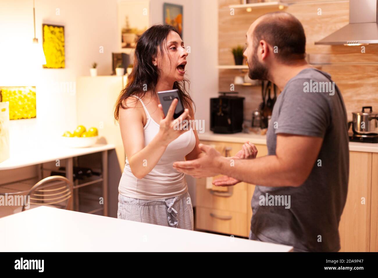 Wife angry with husband because she caught him cheating. Heated angry frustrated offended irritated accusing her man of infidelity showing him messages on smartphone yelling desperate. Stock Photo