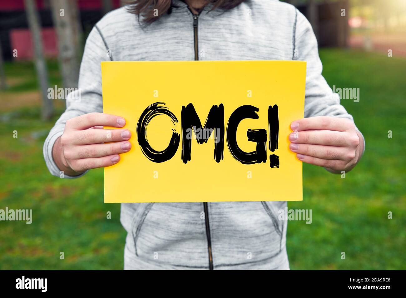 Male teenager holds a yellow banner with the abbreviation OMG (oh my god) message against nature background. Stock Photo
