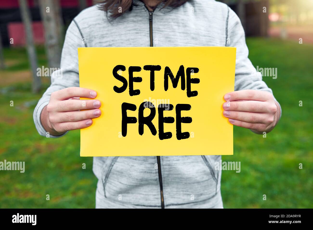 Male teenage boy holds a yellow banner with set me free text against nature background. Freedom and independence in puberty. Stock Photo