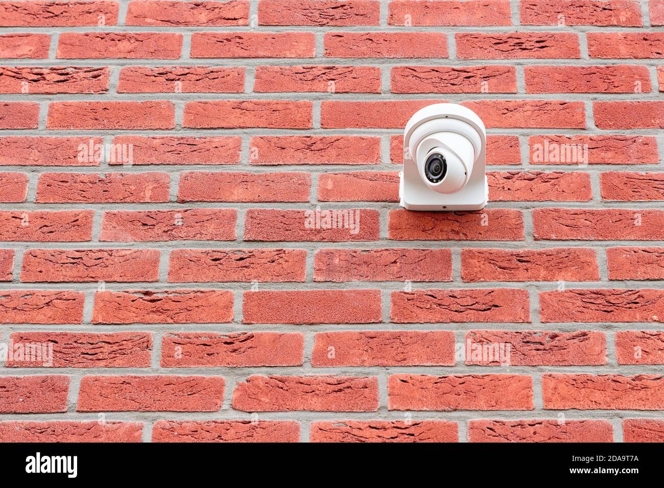 Low angle view on white cctv security camera mounted on a red brick wall. Security concept, big brother is watching Stock Photo