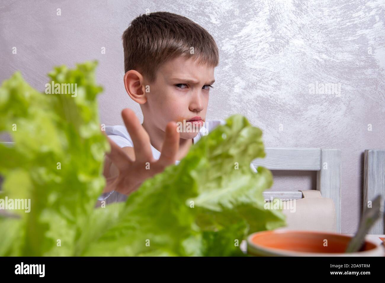 A Caucasian boy refuses to eat salad, with an open hand makes a stop sign with a confident expression on his face, a gesture of protection, refusal to Stock Photo