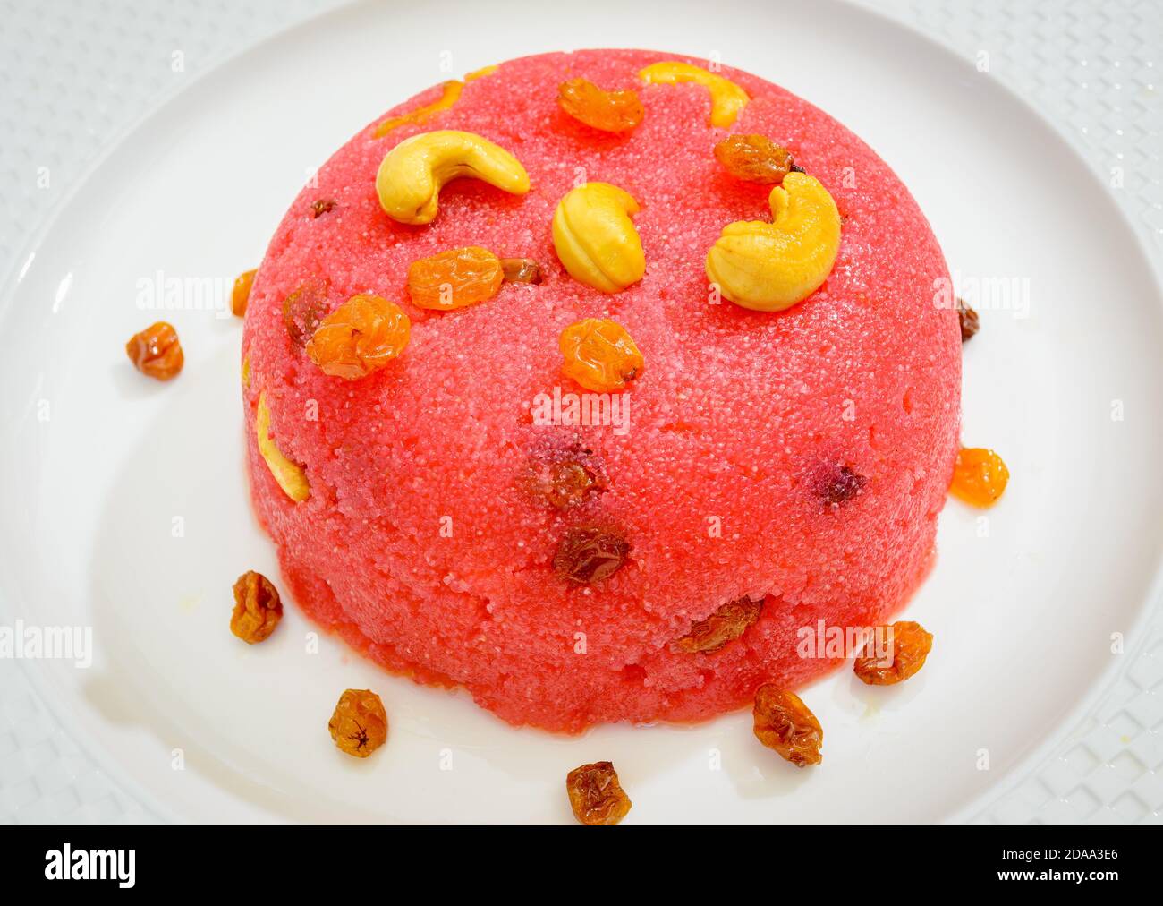 Beautiful, ready-to-eat Pink Rava Kesari mound in a white plate garnished with cashew nuts & raisins Stock Photo