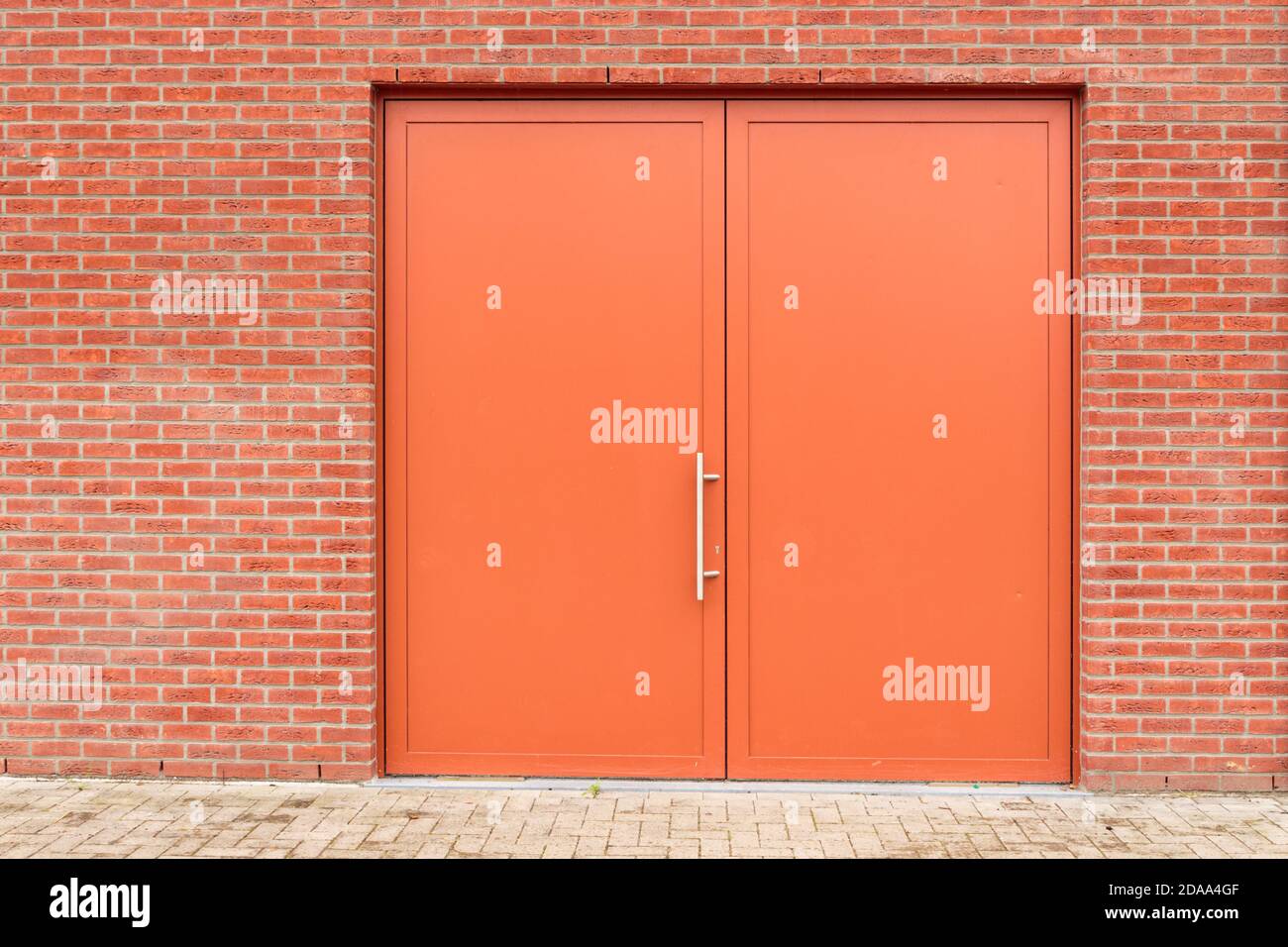 Industrial orange brown metal double swinging closed door in red brick wall. Background replacement Stock Photo