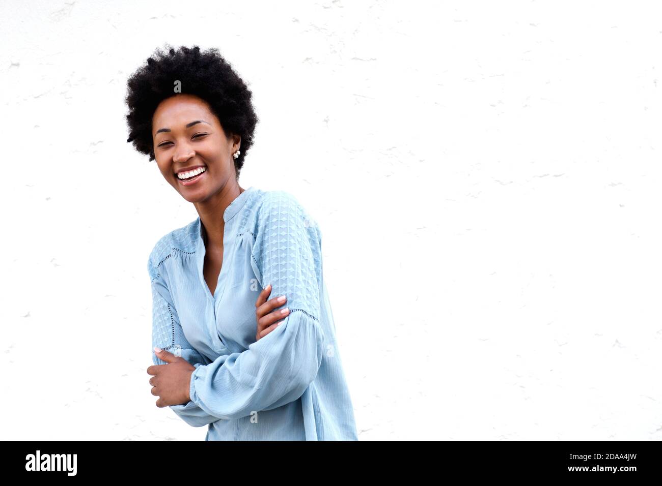 Portrait of smiling young black woman standing with her arms crossed ...